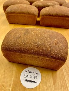 Unsliced loaves of fresh bread with a The Bread Lab Collective coaster.