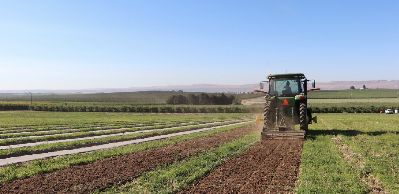 image shows a tractor pulling a rototiller attachment making individual tilled rows.
