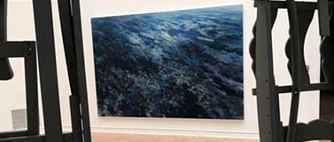 “Spoiled Landscapes – Ocean,” an oil on canvas by Baorong Liang, is seen through a gap in Brighton McCormack’s house-like structure “Fully Furnished” (in video above) at the 2019 MFA + MDes Thesis Exhibition at the Henry Art Gallery.