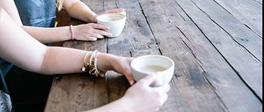 Two people sit at a wooden table with coffee cups.
