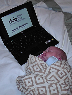 Newborn wrapped in blanket next to laptop displaying DUB group logo