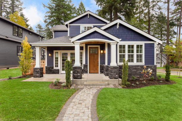 Modern suburban house with blue siding, stone accents, white trim, and a landscaped front yard with young trees and a paved walkway
