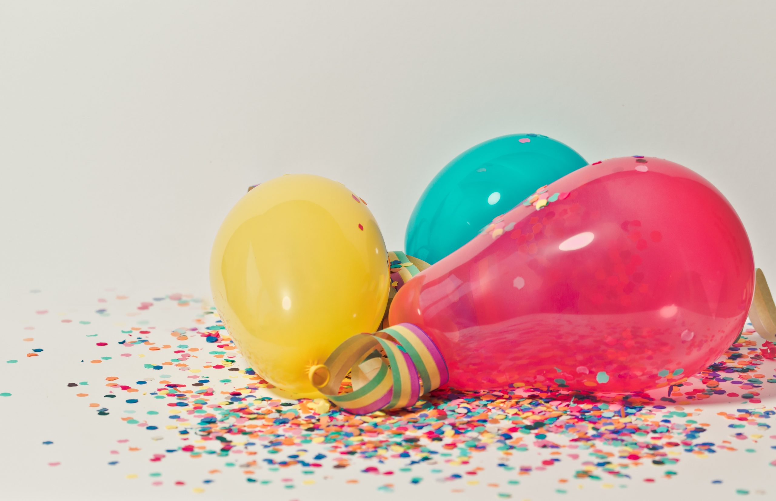 yellow, teal, and hot pink balloons rest on confetti and streamers