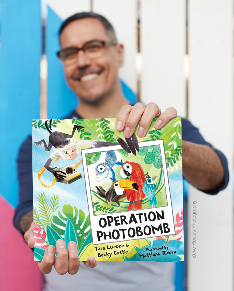 Illustrator Matthew Rivera holds book Operation Photobomb; the cover features toucan, parrot, cotinga and chameleon in a photograph being held by the character monkey