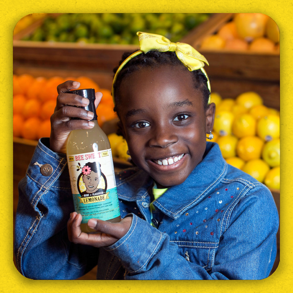 A grinning black girl holding a bottle of her lemonade