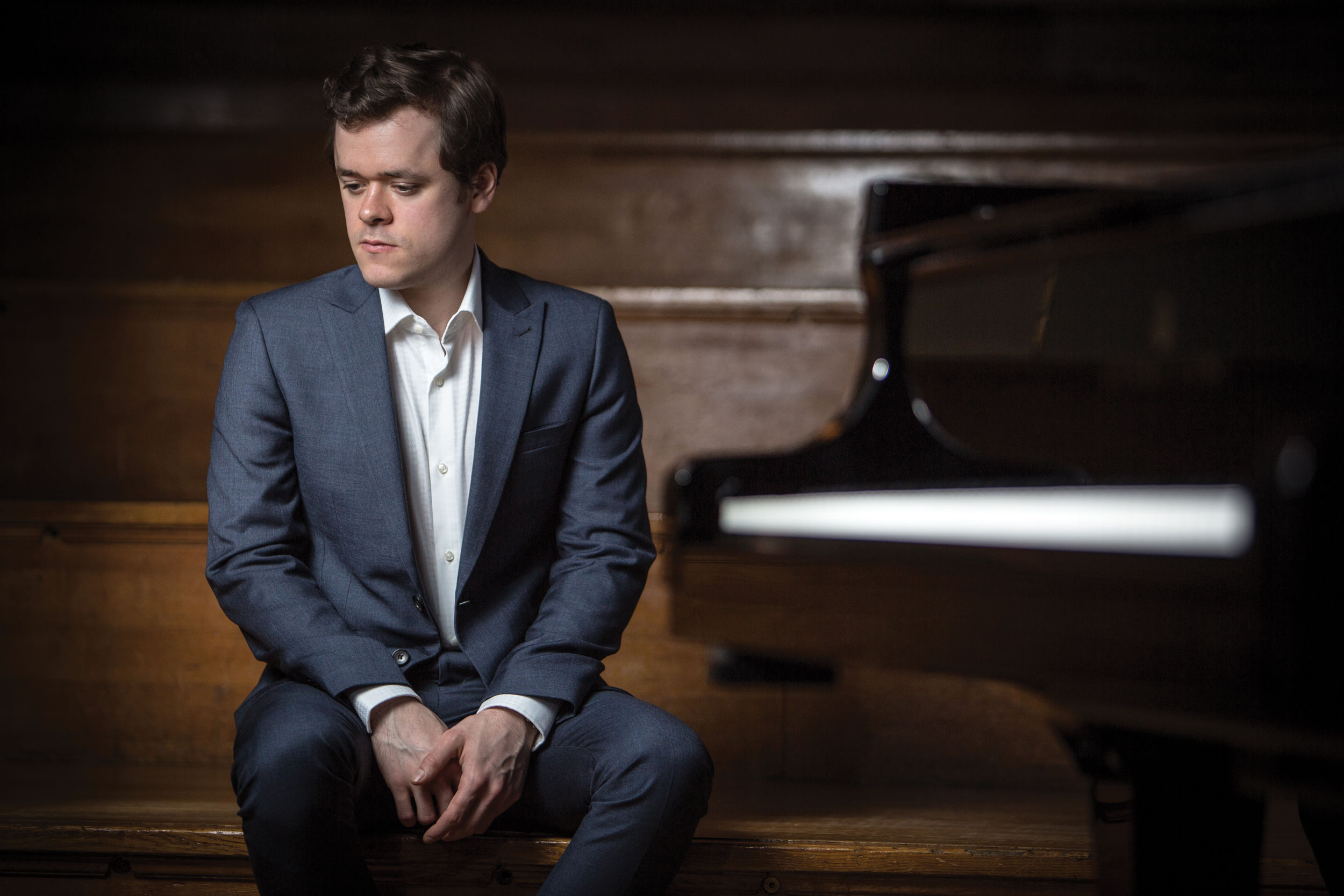 man in blue suit sitting on stairs with piano in the background
