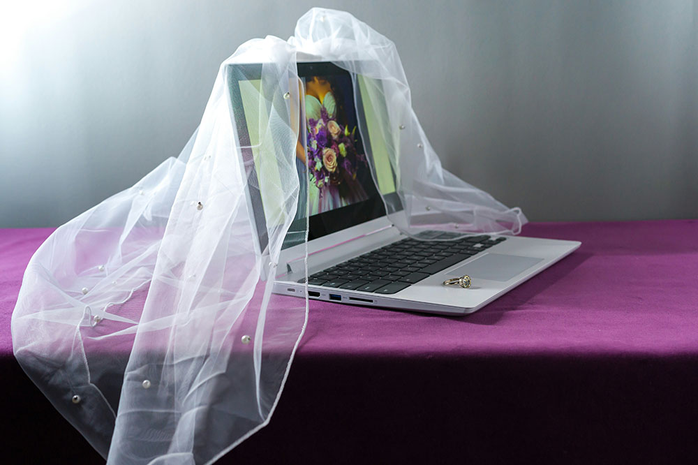 Laptop with bride shown, a wedding veil and ring are draped over the laptop