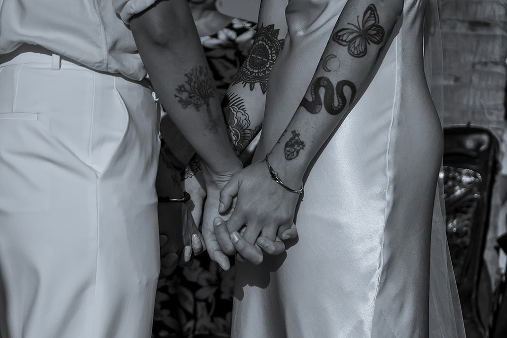 Close up photo shows two people holding hands on the wedding day with tattoos