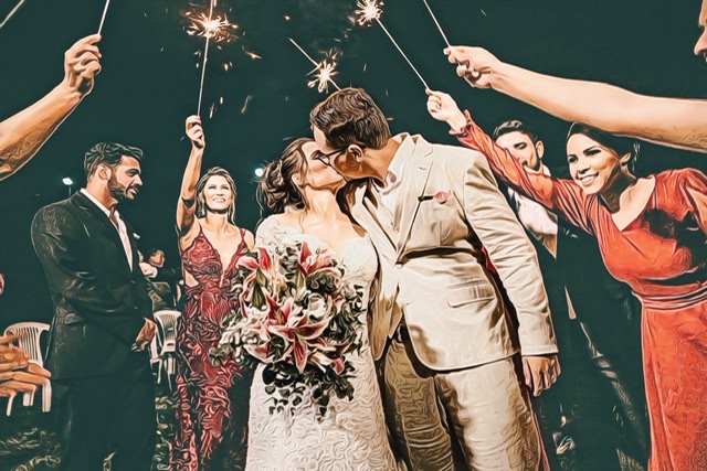 Newlyweds kiss on the wedding day after their ceremony as friends and relatives hold up sparklers in celebration.