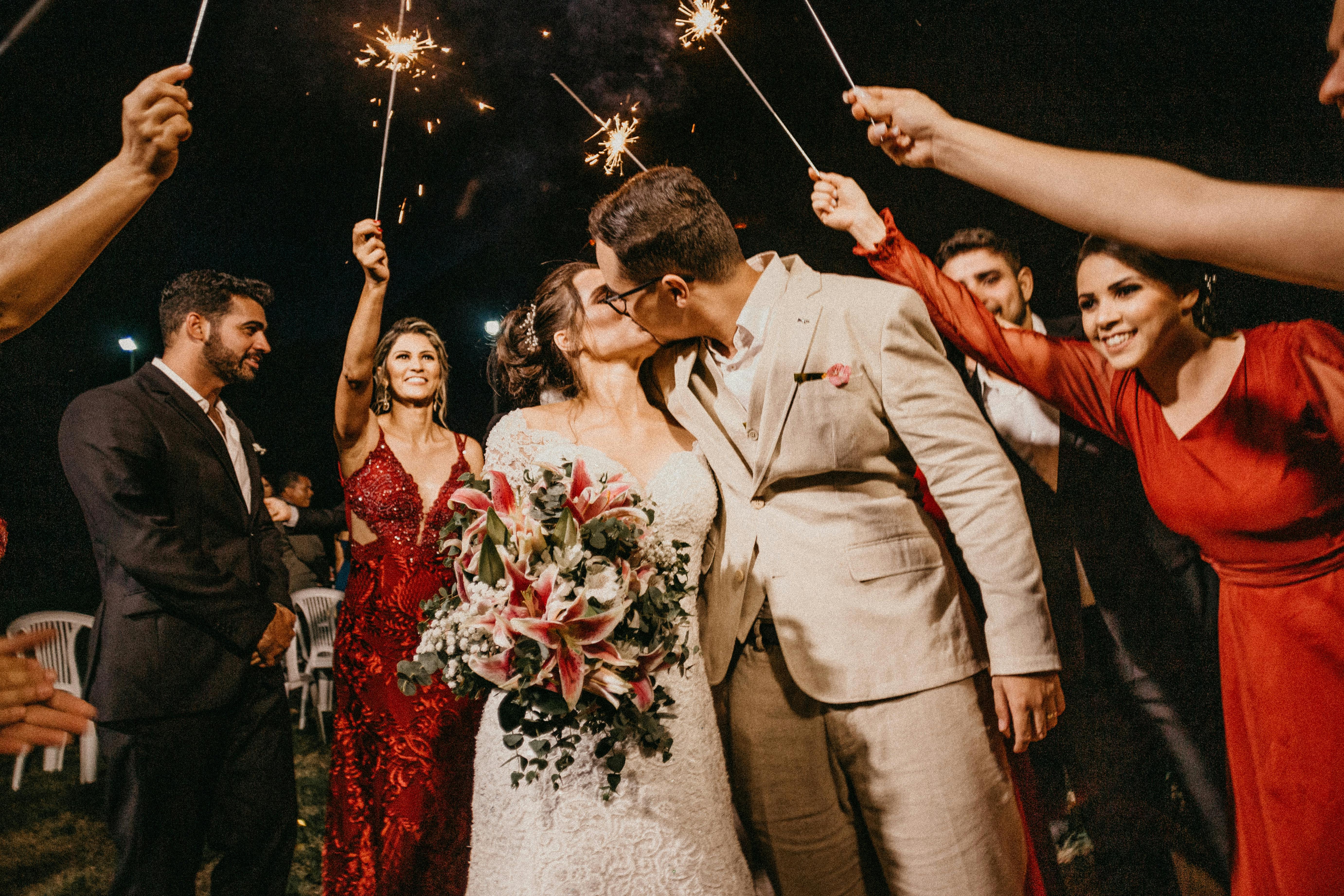 Newlyweds kiss on the wedding day after their ceremony as friends and relatives hold up sparklers in celebration.