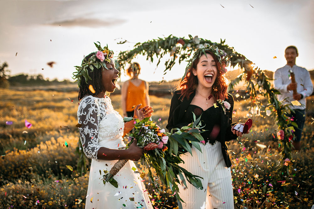 Brides at a summer solstice wedding, outdoors in a field, happy, wearing flower head wreaths