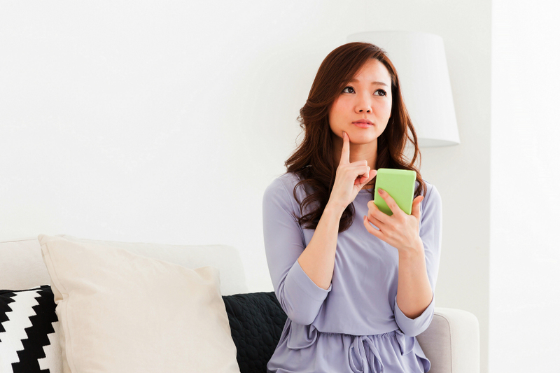 image is of a young woman, wedding officiant, looking contemplative as she holds her phone up ready to dial the local county clerk office to register