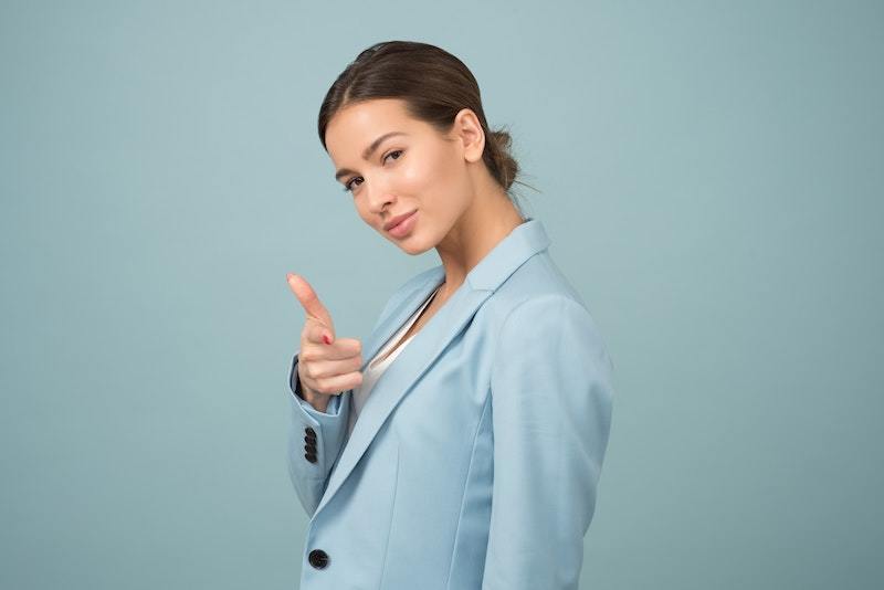 image is a photograph of a young woman looking at the camera and smiling, with her hand up in a gesture to say 'You can do this!' as an encouragement for public speaking