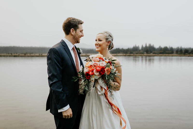 A bride and groom smile and embrace each other in their wedding clothes as the sky behind them is filled with dense wildfire smoke