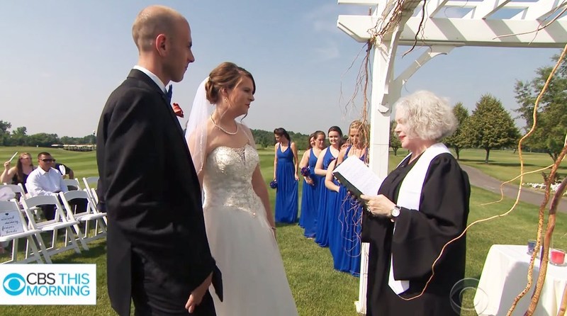 Image is a photograph of an AMM Minister Florence Hunt marrying a young couple outdoors, there is a clear blue sky behind them and everyone looks happy