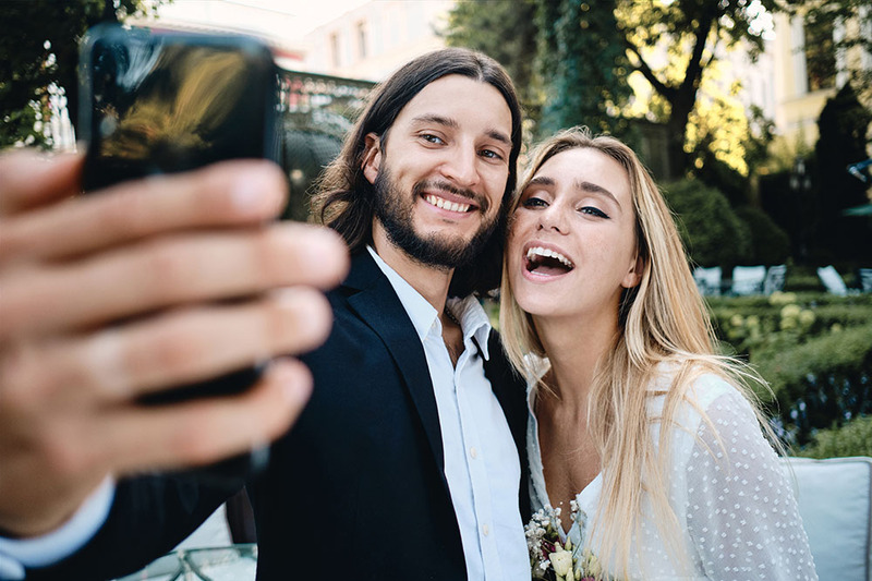 A young couple pose for a wedding selfie outdoors, wearing wedding clothes