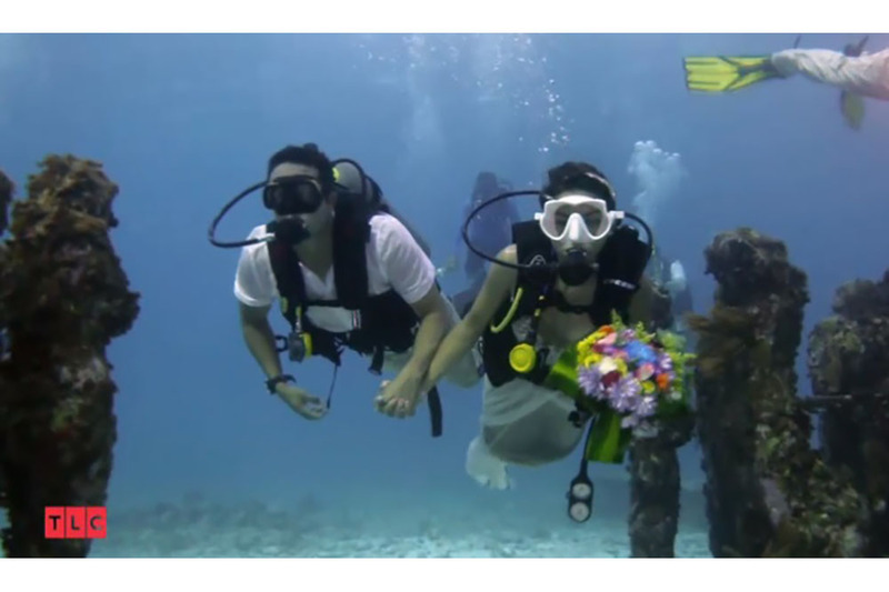 This is a screenshot from the TLC show Say Yes to the Dress, which shows a couple underwater in wedding clothes as part of their ceremony, and the bride is wearing white wedding goggles