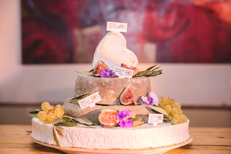 A cheese wheel wedding cake with figs and flowers, the top layer is in the shape of a heart