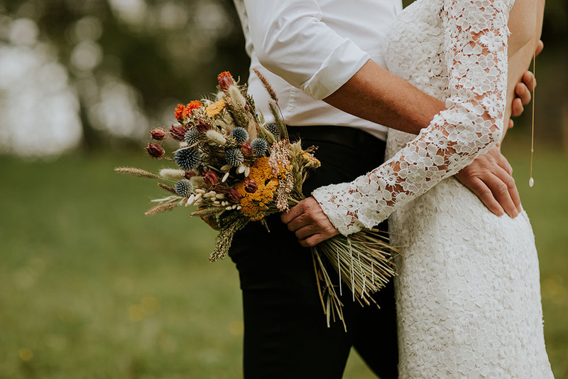 couple in wedding attire hold a colorful bouquet outdoors