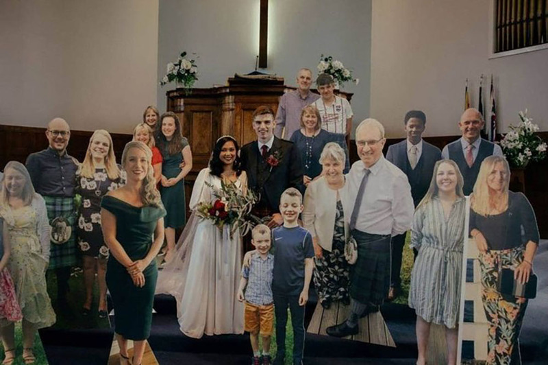Photo via Daily Record, this is a group photo of the MacIver family. The bride and groom stand surrounded by smiling full size cut outs of their family members, including children.