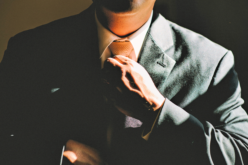 A man straightens his tie as he gets dressed to officiate a wedding