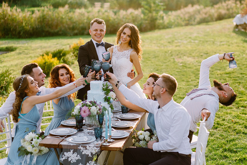 Friends enjoying a beautiful boho chic themed wedding reception dinner outdoors, sitting around a rustic table in a field 