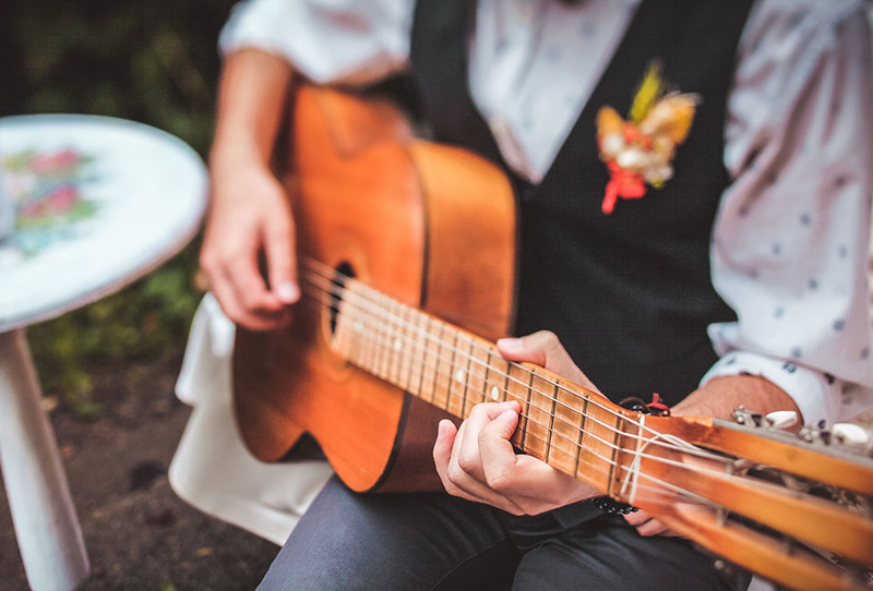 Close up of a young man planning guitar during an outdoor wedding ceremony