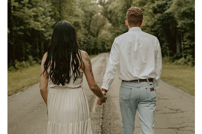 A couple stand in wedding clothes facing away from the camera during their secret outdoor wedding ceremony in the woods