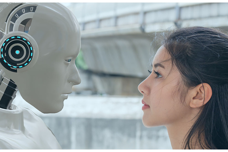 A young woman stands facing a white robot 