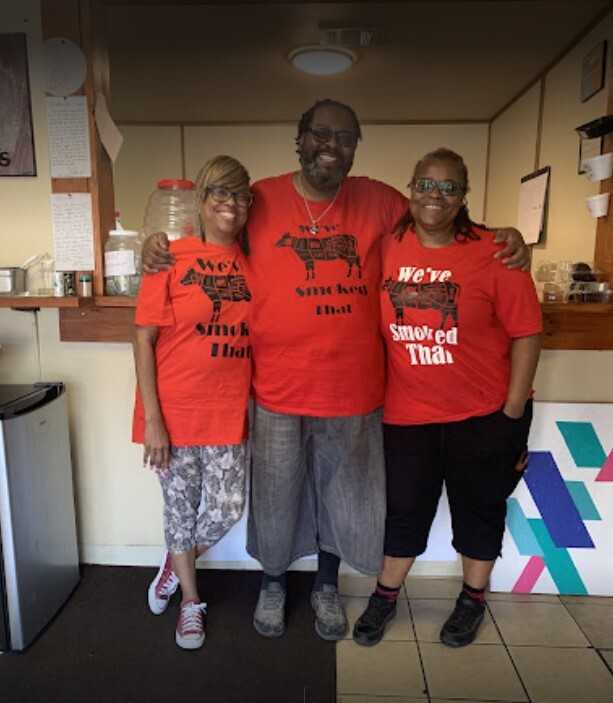 Photo from Jube's Smokehouse website gallery showing three employees in bright red shirts smiling together in the Jube's restaurant