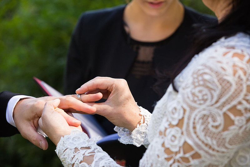 Close up photo of a wedding officiant conducting a ceremony, as the bride places a ring on her partner's finger