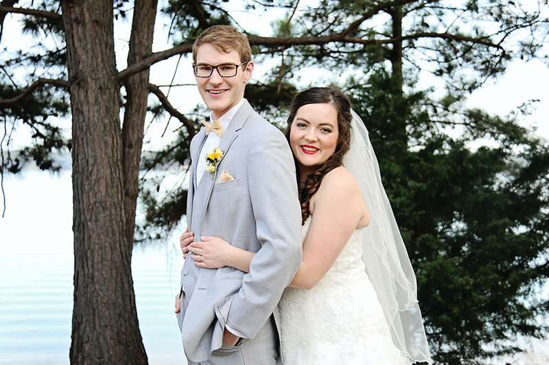 Young newlyweds embrace outdoors on their wedding day in front of large pine trees