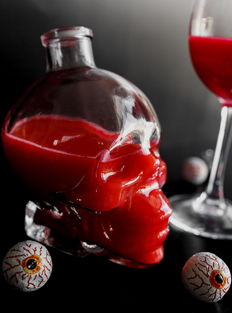 Fake blood in a skull shaped bottle and wine glass, with candy wrapped in foil on the table to look like eyeballs