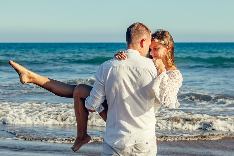 Newlyweds on the beach, the groom carries the bride in his arms