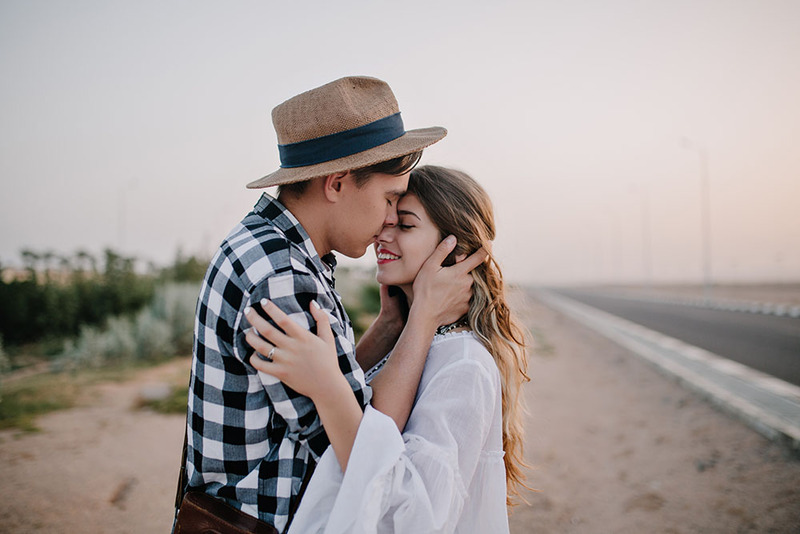 Young newlyweds kiss outdoors in the sunset