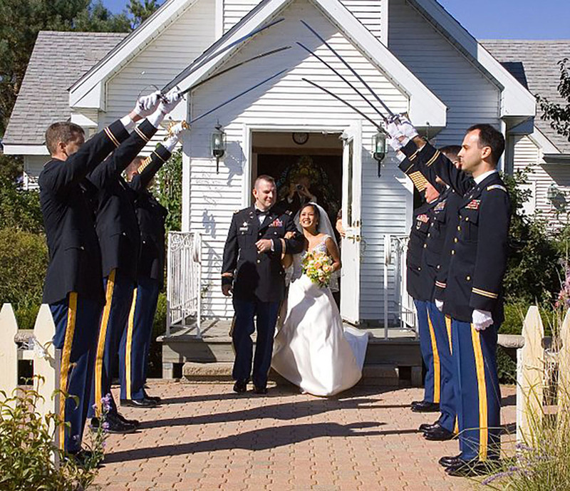Wikimedia Commons image of a newly married couple exiting a small white church while military members hold up their swords to form an arch over the aisle