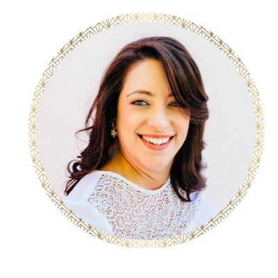 A portrait photo of Renee Dalo, owner and lead wedding planner at Moxie Bright Events. Renee has shoulder length brown hair and a open smile, and is wearing a white lace blouse