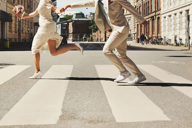 A bride and groom run down a city street in their wedding clothes