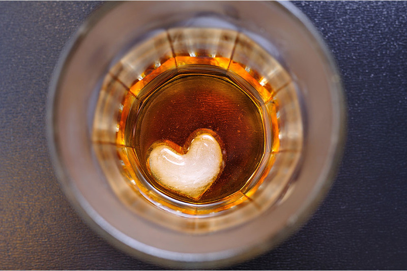 A wedding toast! Close up on a glass of bourbon with a heart shaped piece of ice