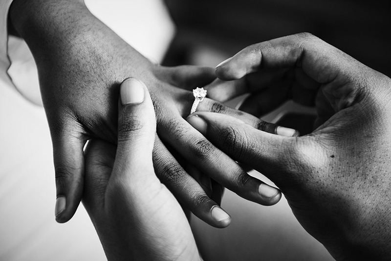 Close up black and white photo of a groom placing a wedding ring on the bride's hand