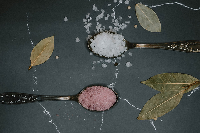 Close up photo of spoons holding two types of salt, sea salt and pink salt