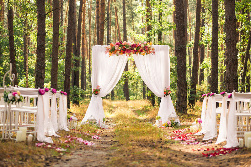 An outdoor wedding ceremony set up in the woods, with an arch and chairs arranged before the ceremony