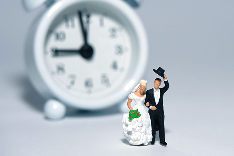 Staged image of a bride and groom figurine set in front of an alarm clock