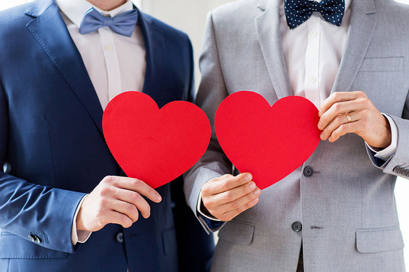 A cute couple in wedding suits hold up two red hearts to celebrate their valentine's day wedding