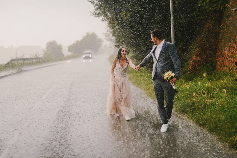 A couple laugh and smile in the rain on the wedding day