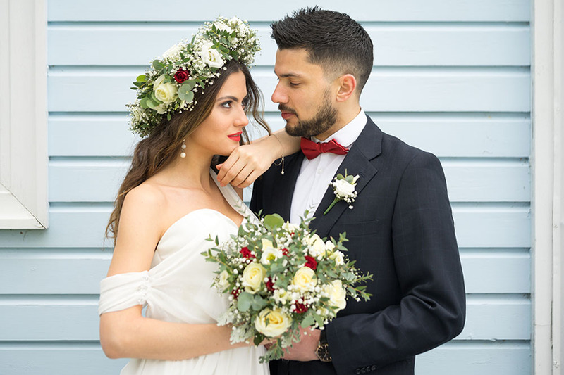 Bride wears a floral head wreath and groom wears a wedding suit, while they pose looking into each other's eyes and smiling