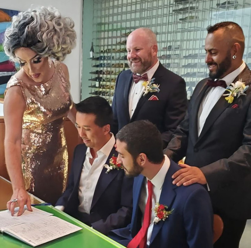 Officiant & Drag Performer Cherri, aka Andy Althoff-Burrows helps two newlyweds sign the marriage license