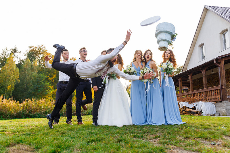 Funny photo shows a groomsman tripping on the grass while carrying a wedding cake, and the cake goes soaring! While the wedding party and newlyweds watch in surprise.