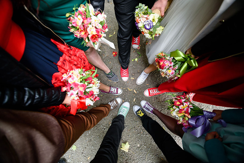 The wedding guests and bride and groom stand in a circle with their feet outstretched to show off their colorful sneakers, taken from above 