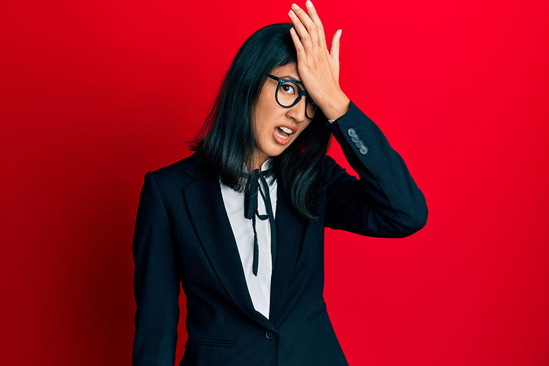 Against a red background, a Wedding officiant in a dark suit holds a head up to her forehead in a gesture that implies "OH no!"